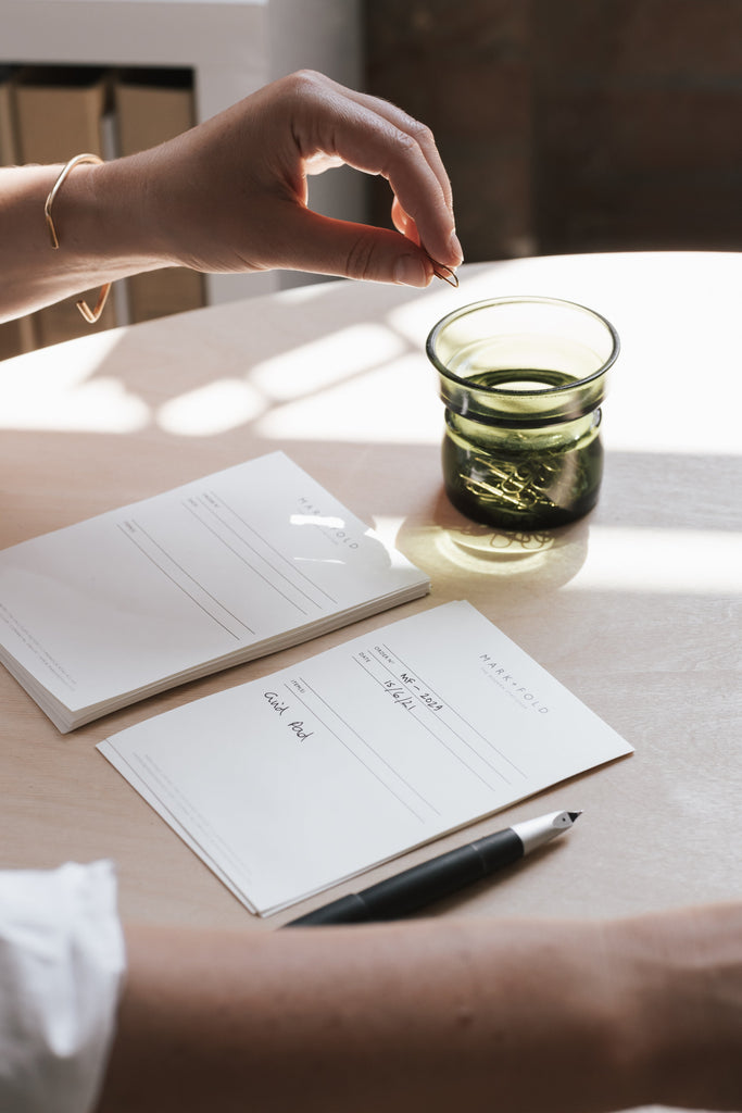 A woman holding a paper clip with a Mark + Fold weekly planner
