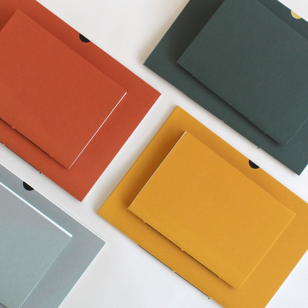Colourful notebooks in A5 and A6 pairs, in rust red, sequoia grey-green, mustard-yellow, and lichen grey on a white background