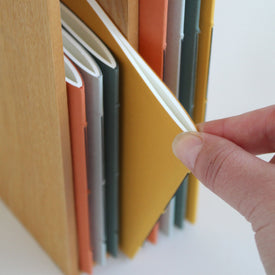 Hand taking a slim notebook from a wooden shelf with colorful notebooks.